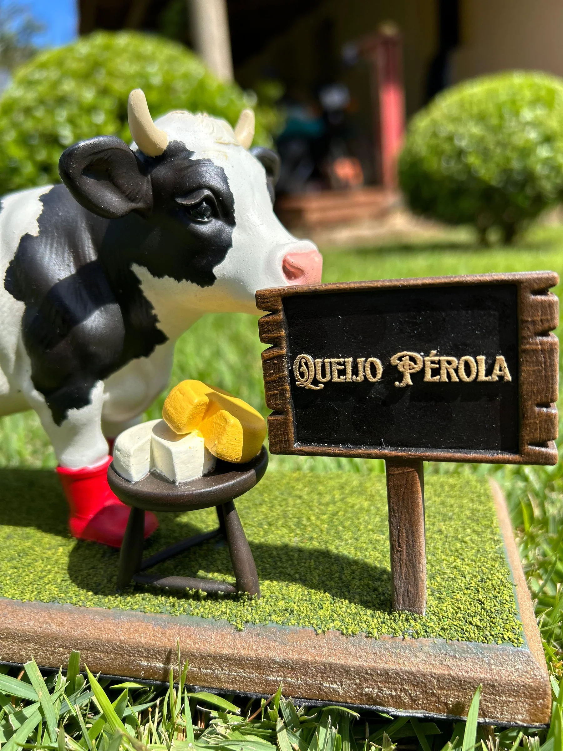 Mascote da Queijo Pérola ao lado da placa da marca